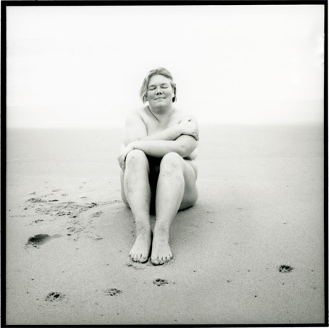 image of performer petra kuppers nude on a beach with her arms wrapped around her