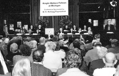 Panelists address half the crowd; overflow attendees watched a big screen monitor.